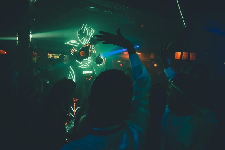 Unrecognizable person in futuristic costume with neon lights making show in dark nightclub near dancing people