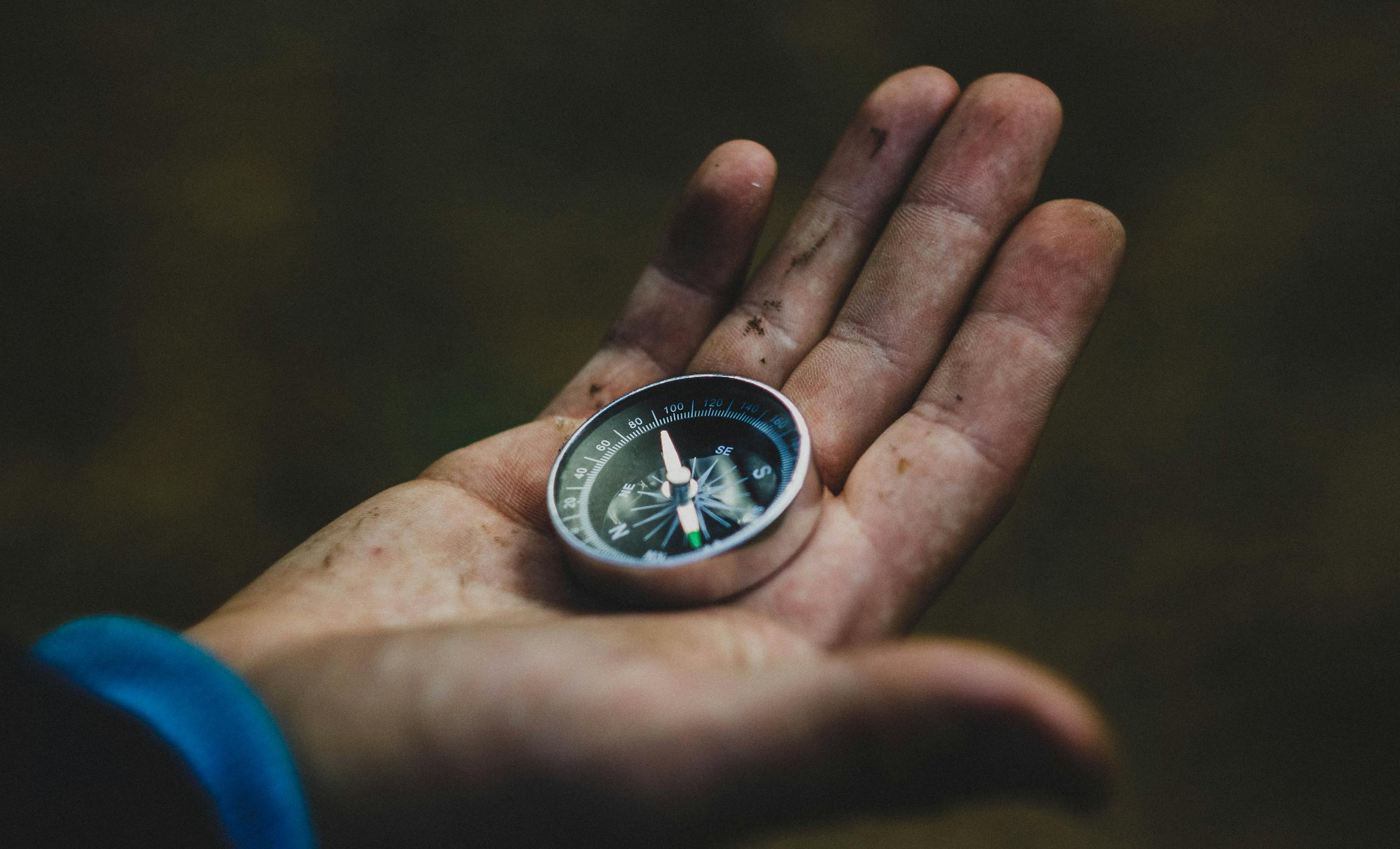 A close-up of a compass held in a dirty hand, symbolizing adventure and navigation.